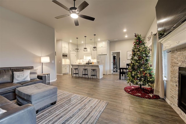 living room with a stone fireplace, ceiling fan, and sink