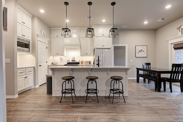 kitchen featuring decorative light fixtures, white cabinetry, stainless steel appliances, and an island with sink