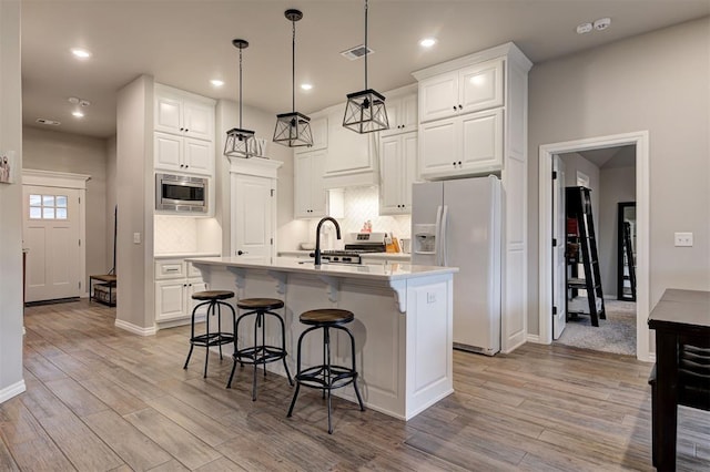 kitchen with appliances with stainless steel finishes, pendant lighting, a center island with sink, light hardwood / wood-style flooring, and white cabinets