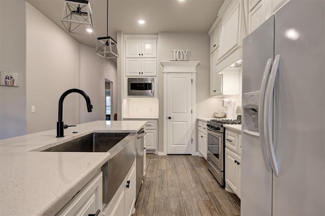 kitchen featuring pendant lighting, hardwood / wood-style flooring, light stone counters, white cabinetry, and stainless steel appliances