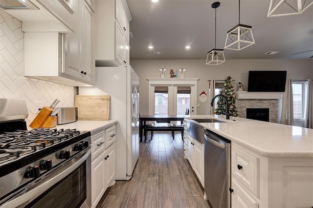 kitchen featuring sink, hanging light fixtures, light hardwood / wood-style flooring, white cabinets, and appliances with stainless steel finishes