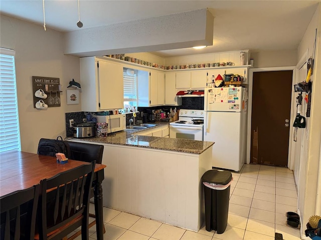 kitchen with white appliances, light tile patterned flooring, dark stone counters, and kitchen peninsula