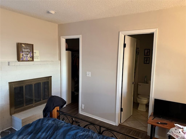 tiled bedroom with ensuite bathroom, a textured ceiling, a fireplace, a spacious closet, and a closet