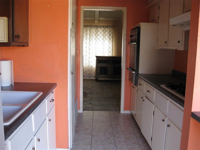 kitchen featuring sink, light tile patterned floors, gas stovetop, black oven, and white cabinets