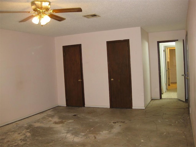 unfurnished bedroom featuring ceiling fan, a textured ceiling, and two closets