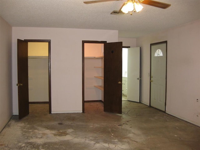 unfurnished bedroom with concrete flooring, a textured ceiling, a walk in closet, and ceiling fan