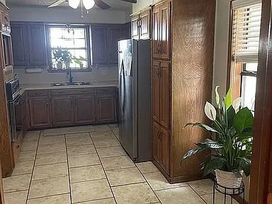 kitchen with sink, ceiling fan, stainless steel fridge, a barn door, and light tile patterned flooring