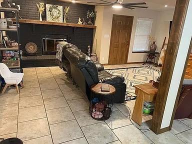 living area featuring ceiling fan, light tile patterned flooring, and a brick fireplace