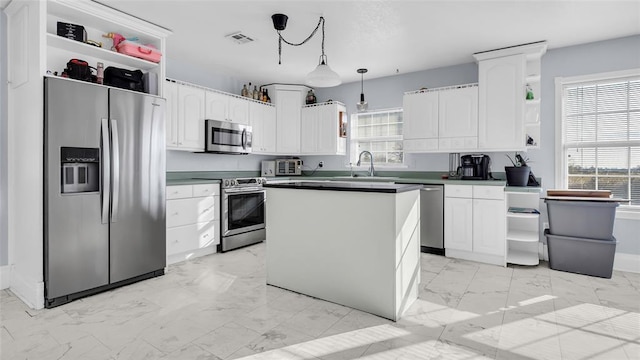 kitchen with stainless steel appliances, sink, white cabinets, a center island, and hanging light fixtures