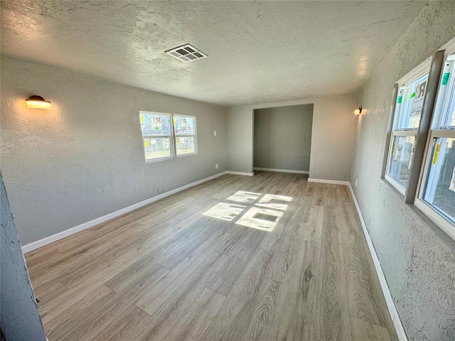 spare room with light hardwood / wood-style floors, a textured ceiling, and a healthy amount of sunlight