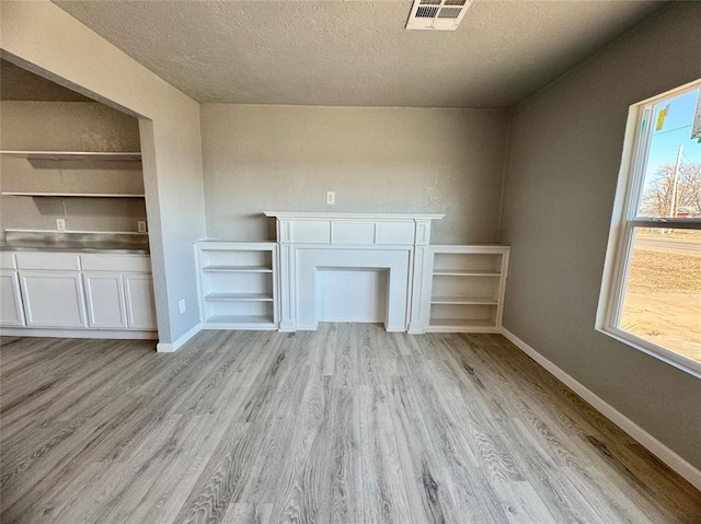 unfurnished living room with a textured ceiling and light hardwood / wood-style floors