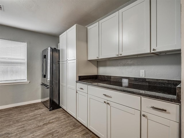 kitchen featuring stainless steel fridge, light hardwood / wood-style flooring, white cabinetry, and dark stone countertops