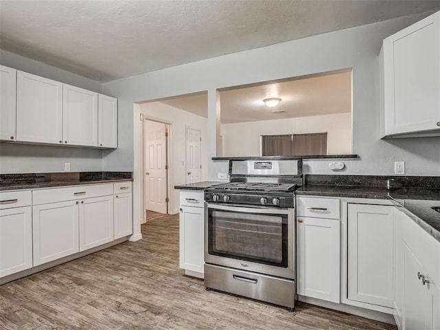 kitchen featuring light wood-type flooring, white cabinetry, dark stone countertops, and stainless steel range with gas stovetop