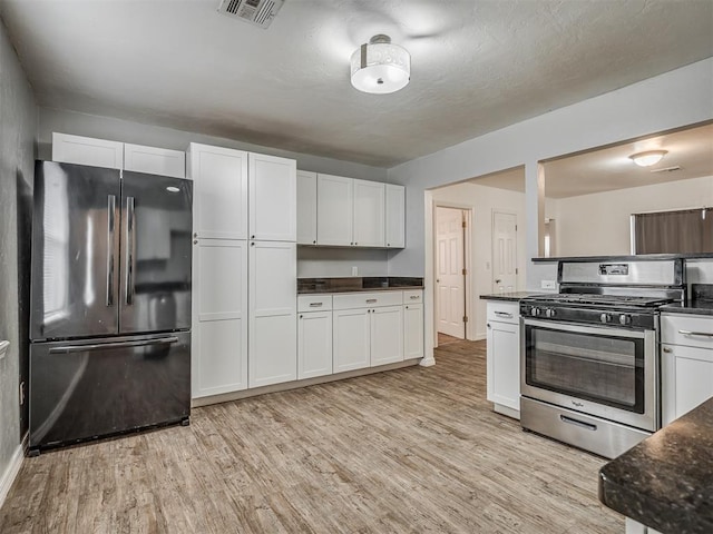 kitchen featuring black refrigerator, light wood-type flooring, white cabinetry, and stainless steel range with gas stovetop