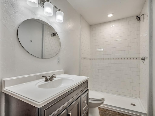 bathroom featuring hardwood / wood-style flooring, vanity, toilet, and tiled shower