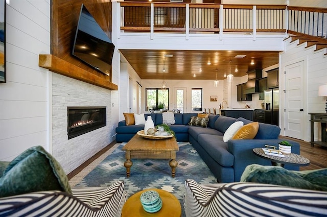 living room with wood walls, a towering ceiling, a fireplace, wood-type flooring, and wood ceiling