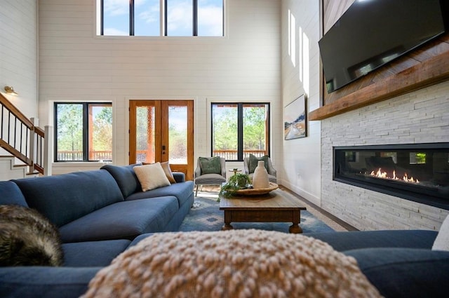 living room with a stone fireplace, a towering ceiling, wood-type flooring, and french doors