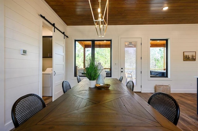 dining area featuring a barn door, washer / dryer, wood ceiling, and wooden walls