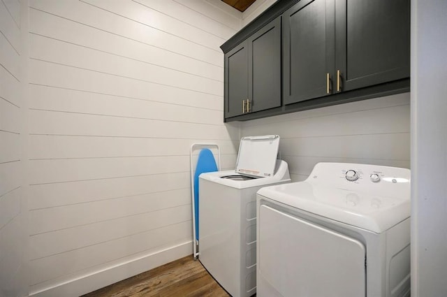 washroom with washing machine and clothes dryer, wood walls, cabinets, and dark hardwood / wood-style floors