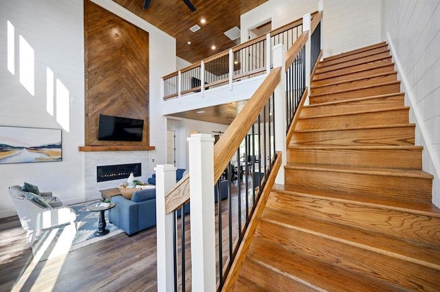 staircase featuring a fireplace, a towering ceiling, wood ceiling, and wood-type flooring