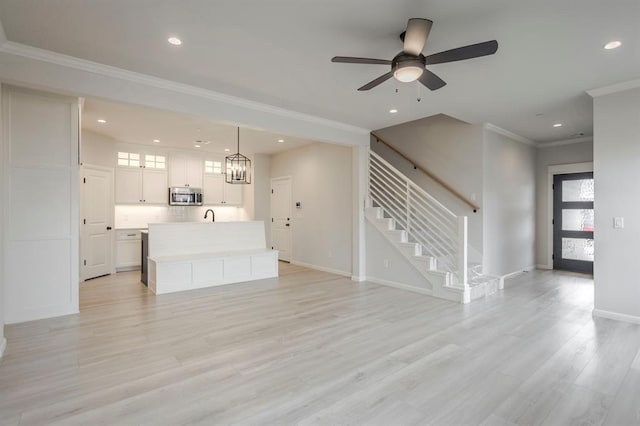 unfurnished living room featuring ornamental molding, light hardwood / wood-style floors, ceiling fan with notable chandelier, and sink