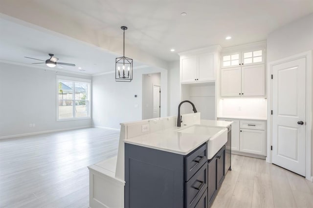 kitchen with ceiling fan with notable chandelier, pendant lighting, white cabinets, sink, and a kitchen island with sink