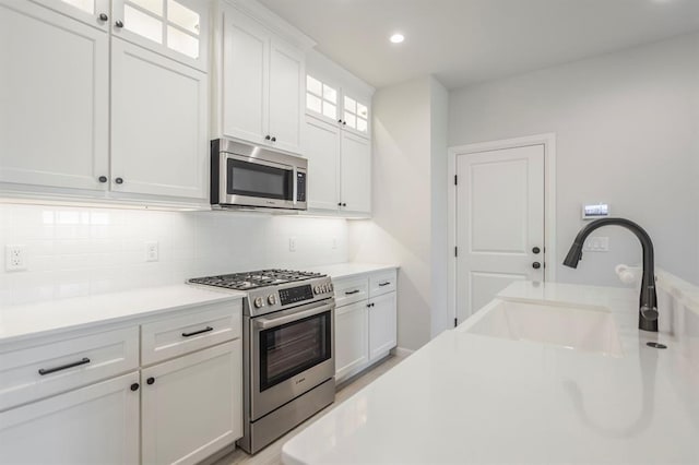 kitchen with tasteful backsplash, white cabinets, appliances with stainless steel finishes, and sink