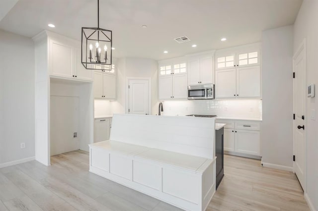 kitchen featuring a notable chandelier, white cabinets, a center island with sink, and decorative light fixtures