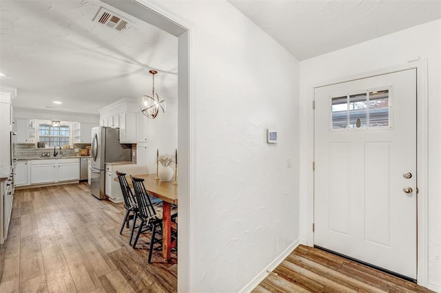 entrance foyer featuring light wood-type flooring, an inviting chandelier, a wealth of natural light, and sink