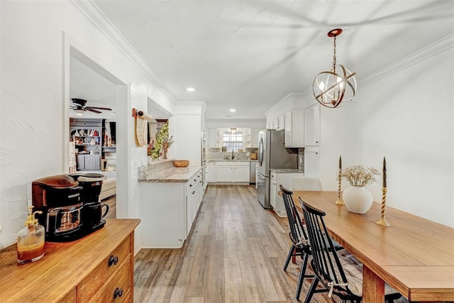 kitchen featuring stainless steel refrigerator, sink, white cabinets, ceiling fan with notable chandelier, and ornamental molding