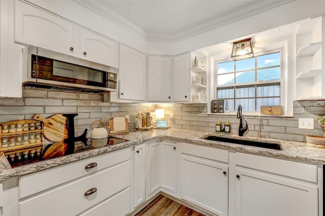 kitchen featuring white cabinets, black stovetop, light stone counters, and sink