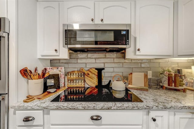 kitchen featuring light stone countertops, black electric stovetop, backsplash, and white cabinetry