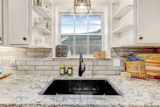 kitchen featuring white cabinetry, decorative backsplash, light stone countertops, and sink