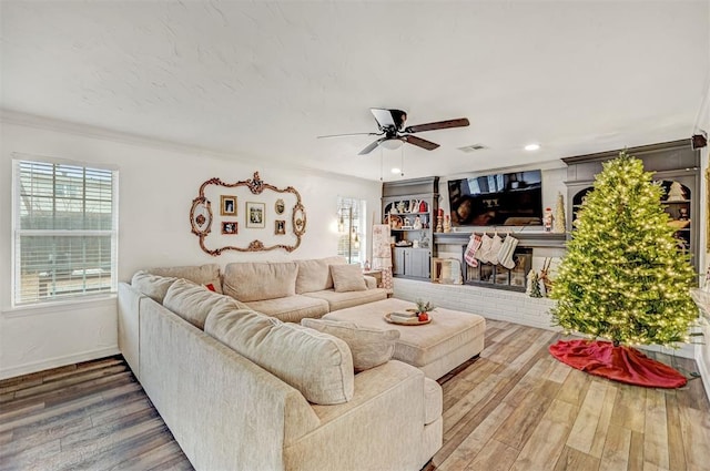 living room featuring hardwood / wood-style flooring, crown molding, ceiling fan, and a brick fireplace