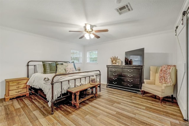 bedroom featuring ceiling fan, light hardwood / wood-style floors, ornamental molding, and a textured ceiling