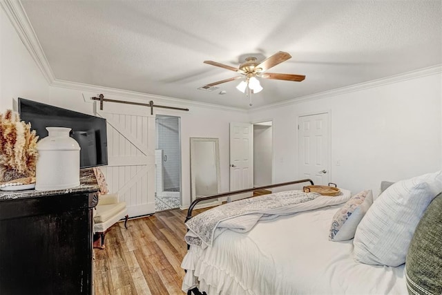 bedroom featuring light wood-type flooring, a barn door, ceiling fan, and crown molding