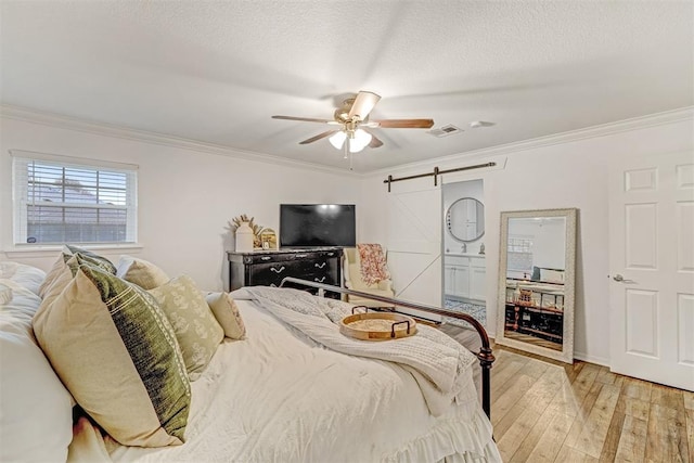 bedroom featuring light hardwood / wood-style flooring, ensuite bath, ceiling fan, a barn door, and ornamental molding