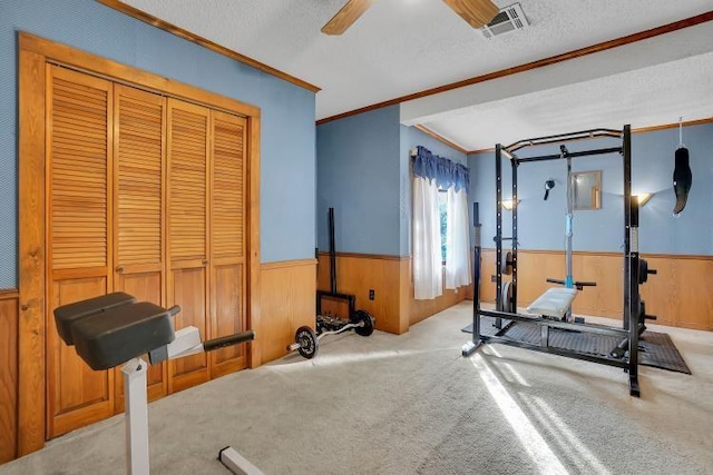 exercise room with a textured ceiling, ceiling fan, crown molding, and light carpet