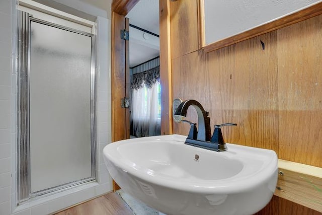 bathroom with wooden walls, hardwood / wood-style flooring, a shower with shower door, and sink