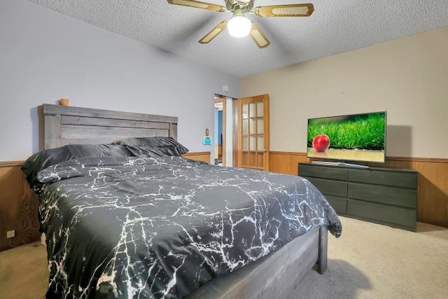 bedroom with wood walls, ceiling fan, light carpet, and a textured ceiling