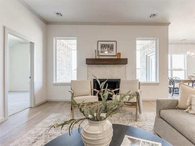 living room featuring light hardwood / wood-style floors, a healthy amount of sunlight, crown molding, and a tiled fireplace