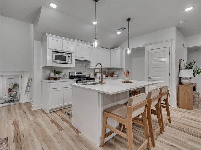 kitchen with white cabinets, hanging light fixtures, tasteful backsplash, light hardwood / wood-style floors, and stainless steel appliances