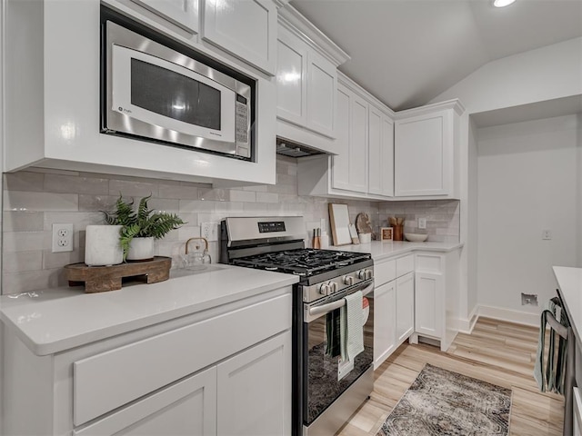 kitchen with light wood finished floors, stainless steel appliances, tasteful backsplash, white cabinetry, and vaulted ceiling