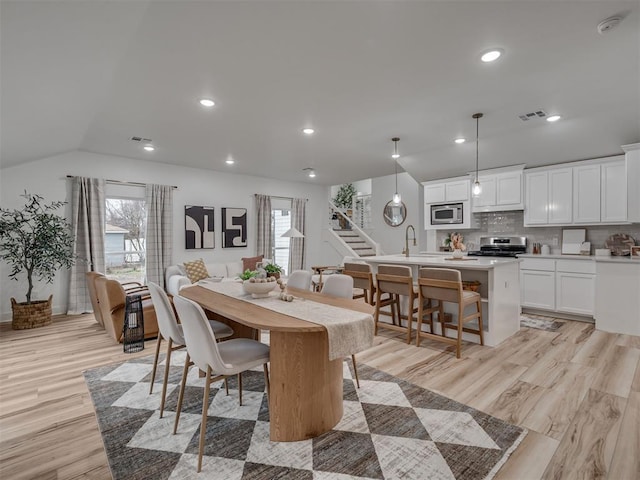 dining room with light wood-type flooring, lofted ceiling, and sink