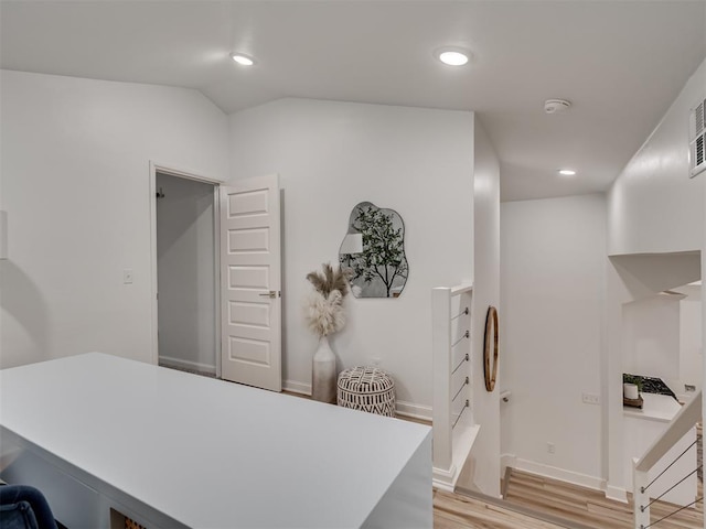 interior space featuring a breakfast bar area, recessed lighting, vaulted ceiling, light countertops, and light wood finished floors