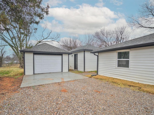 view of side of home with driveway, a shingled roof, a garage, and an outbuilding