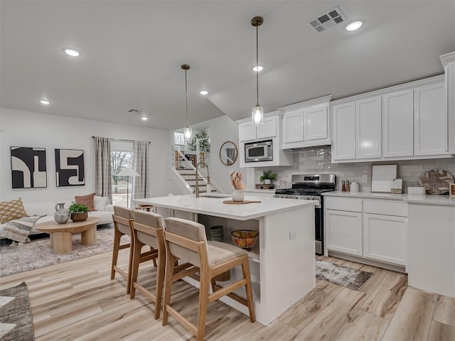 kitchen featuring light wood-style flooring, stainless steel appliances, visible vents, white cabinetry, and backsplash