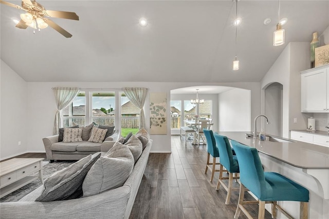 living room featuring dark hardwood / wood-style flooring, sink, ceiling fan with notable chandelier, and vaulted ceiling