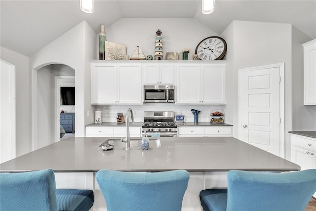 kitchen with a center island with sink, backsplash, appliances with stainless steel finishes, and vaulted ceiling