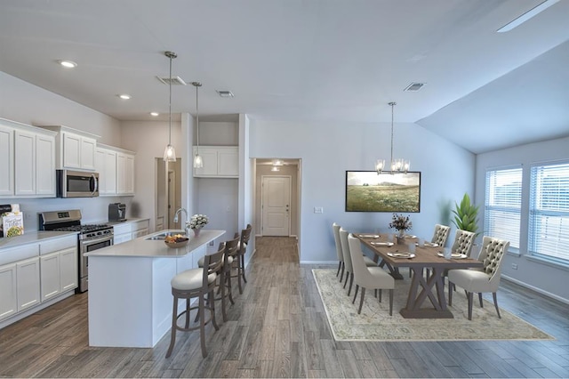 kitchen with sink, appliances with stainless steel finishes, decorative light fixtures, and an island with sink